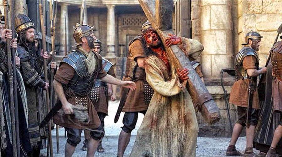 Jesus carrying the cross, surrounded by Roman soldiers.